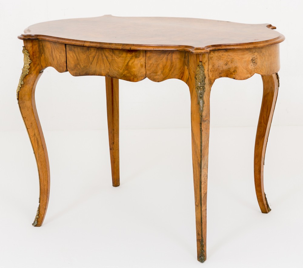 A burr walnut centre table featuring a serpentine-shaped top, cabriole legs, and brass corner mounts against a white background.