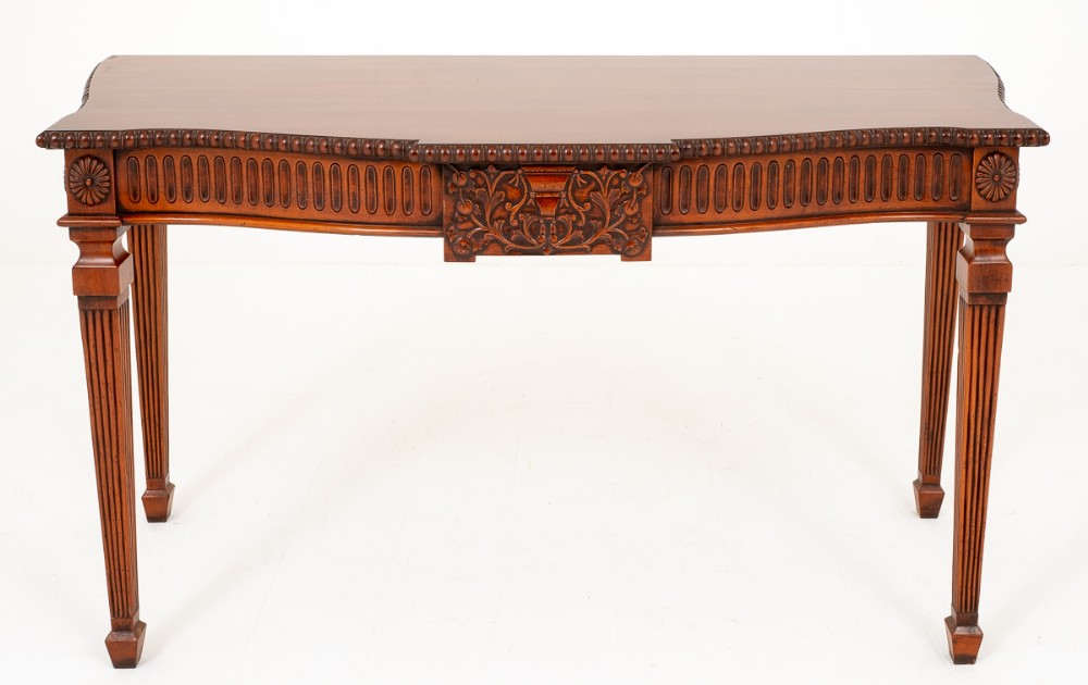 A warm brown carved mahogany side table featuring fluted tapered legs, floral corner rosettes, and an ornate carved central panel beneath a beaded frieze.
