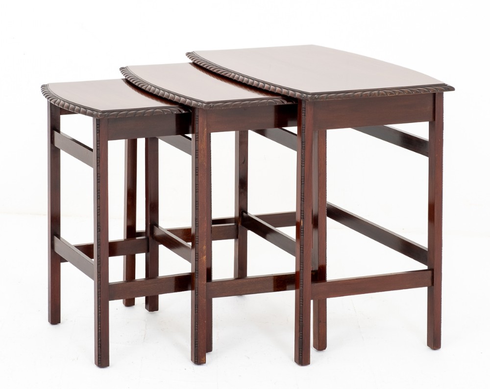 A set of three graduated mahogany nesting tables featuring carved gadrooned edges, square legs, and side stretchers.