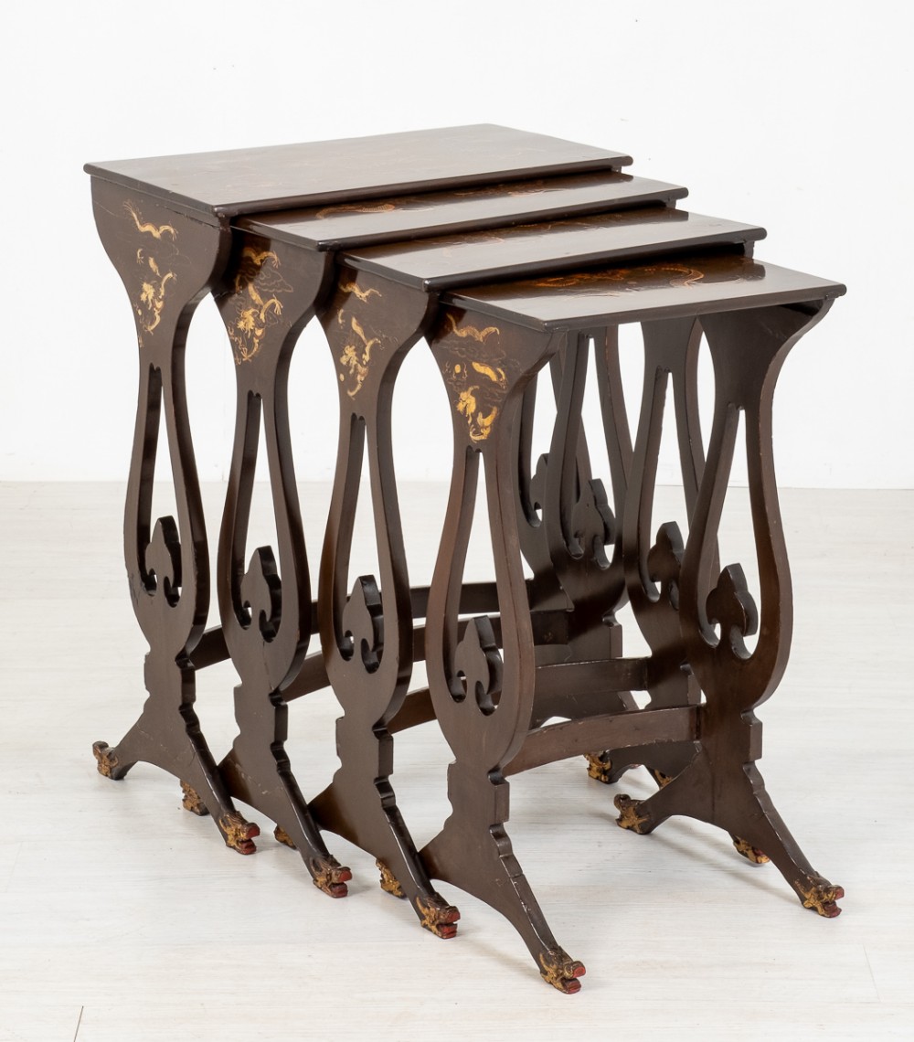 A set of four dark ebonised wooden nesting tables arranged in a descending stepped formation, decorated with gold chinoiserie dragon motifs on top and pierced legs.