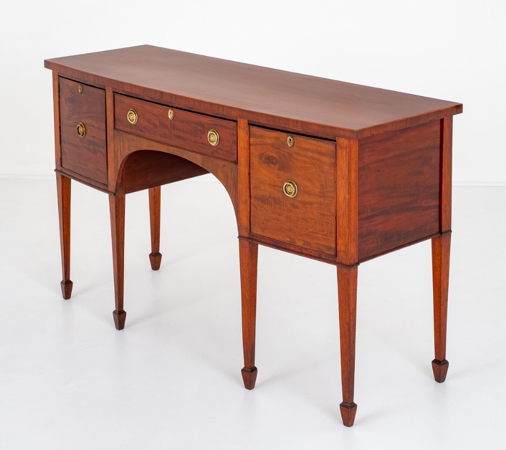 A Georgian style mahogany sideboard featuring square tapered legs with spade feet, brass ring handles, and flame mahogany veneer drawers.