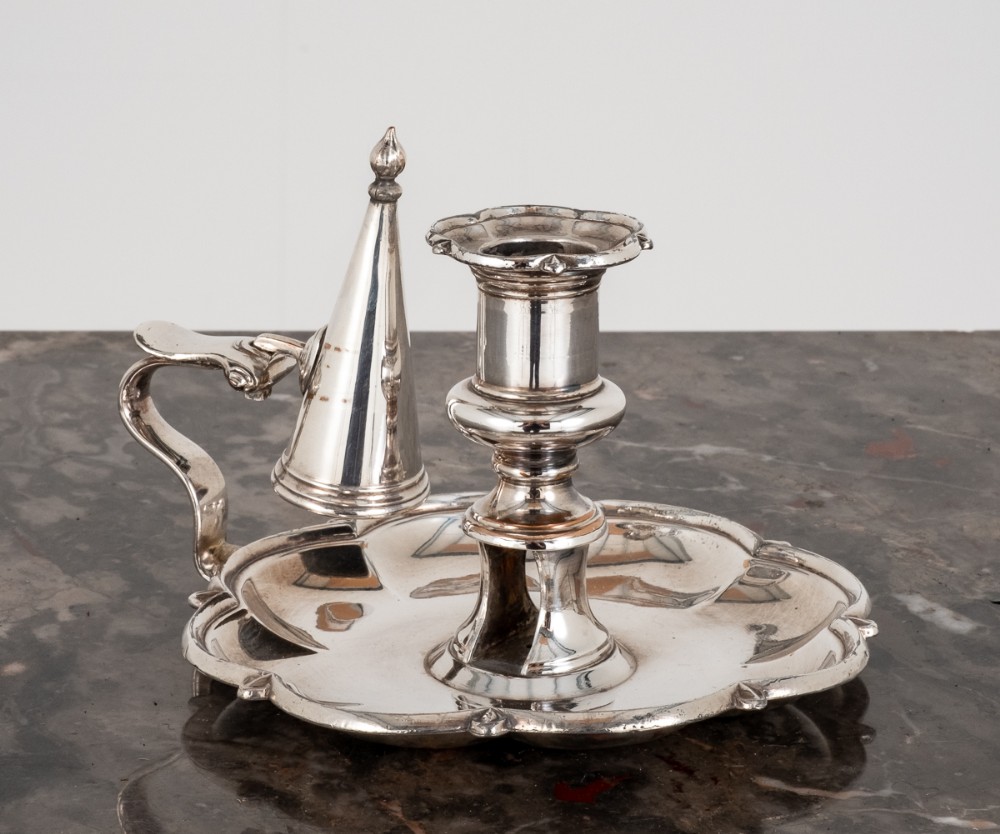 A Georgian Revival silver-plated chamberstick featuring a scalloped tray base, central candle socket, loop handle, and removable conical snuffer.