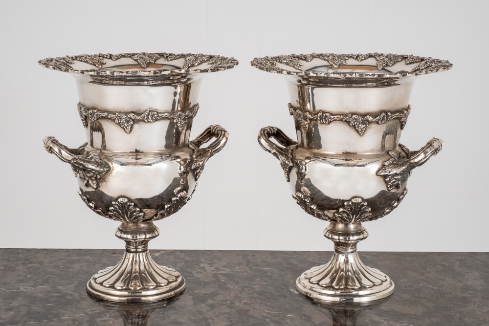 A pair of campana-shaped silver plated wine coolers with twin handles, fluted bases, and relief leaf details around the rim.