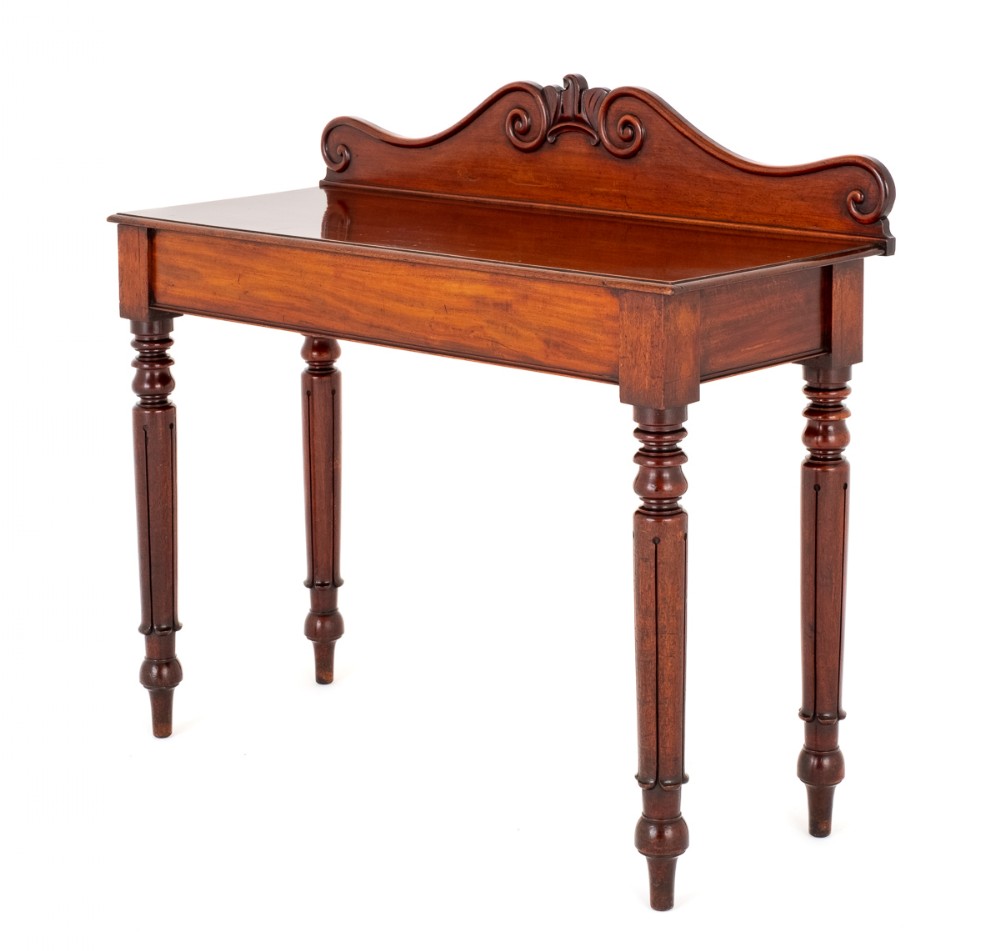 A William IV mahogany console table featuring a carved scrolled backboard gallery and four turned, reeded legs.