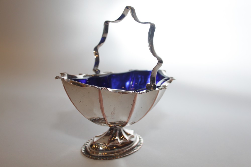 A silver-plated pedestal bon bon dish featuring a scalloped rim, a swing handle, and a cobalt blue glass insert. View III