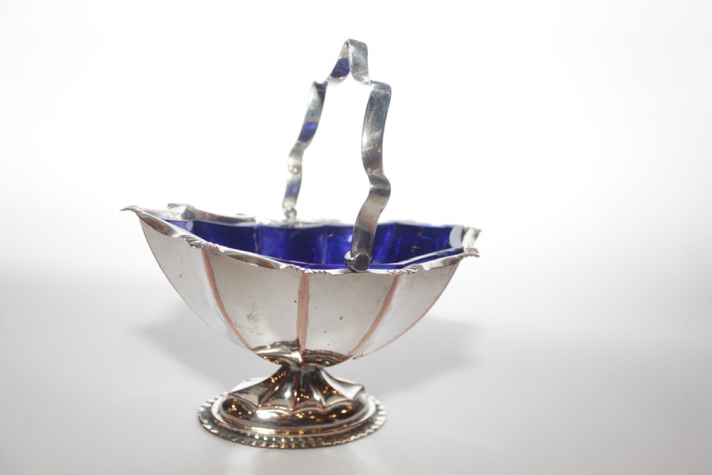 A silver-plated pedestal bon bon dish featuring a scalloped rim, a swing handle, and a cobalt blue glass insert. View II