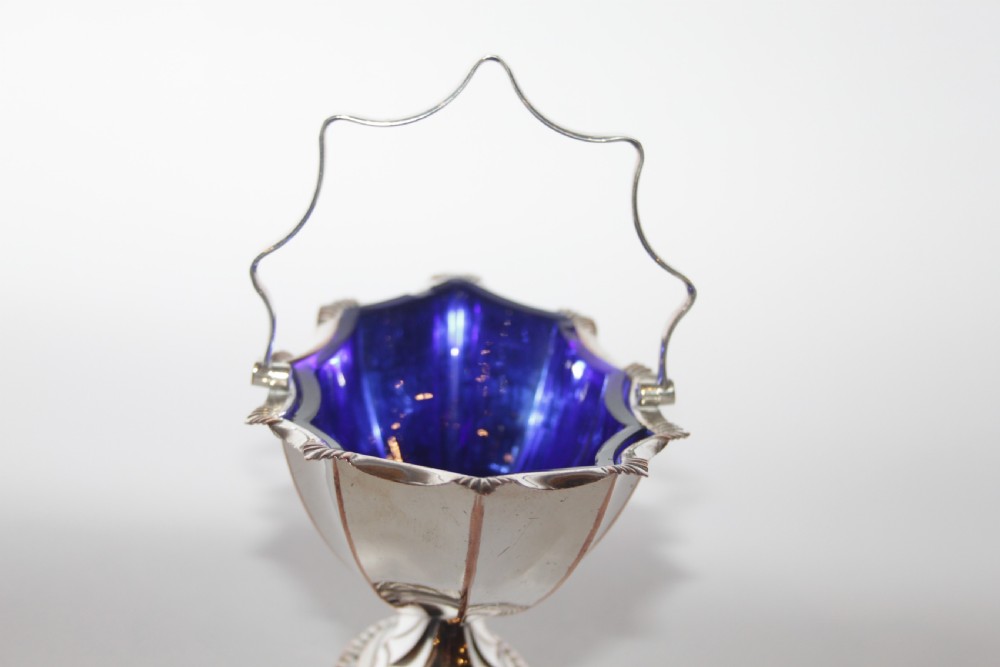 A silver-plated pedestal bon bon dish featuring a scalloped rim, a swing handle, and a cobalt blue glass insert. View V