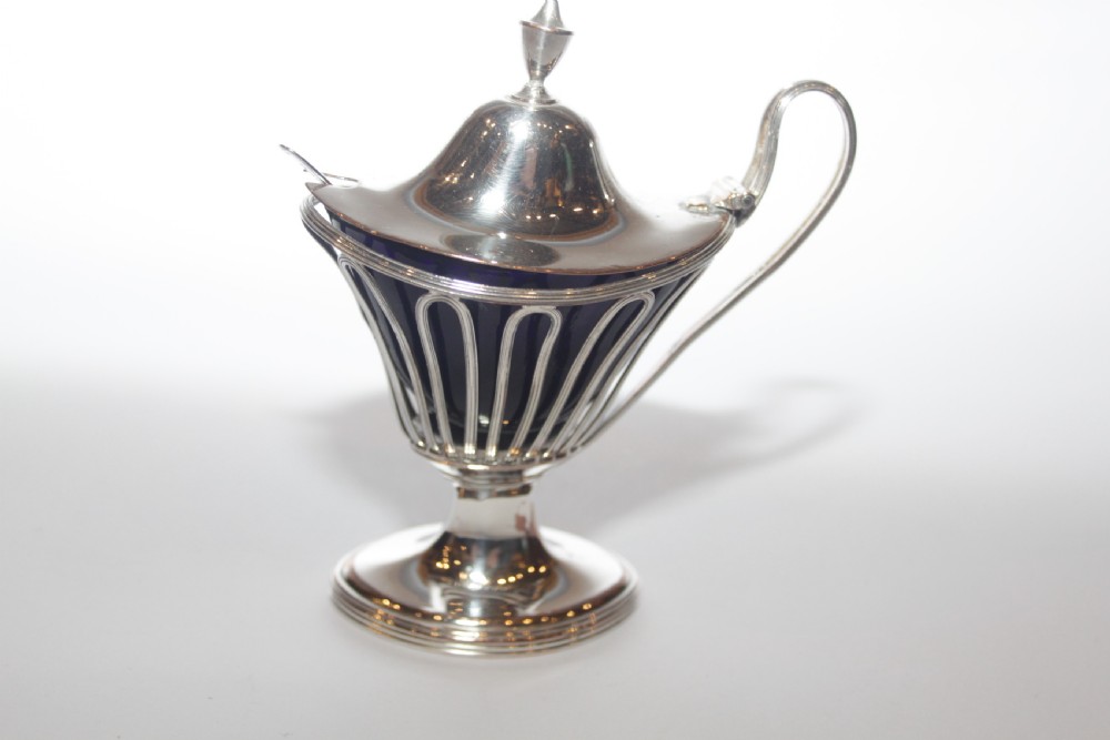 A silver-plated mustard pot with a pedestalled base, looped handle, conical lid, and removable cobalt blue glass liner.