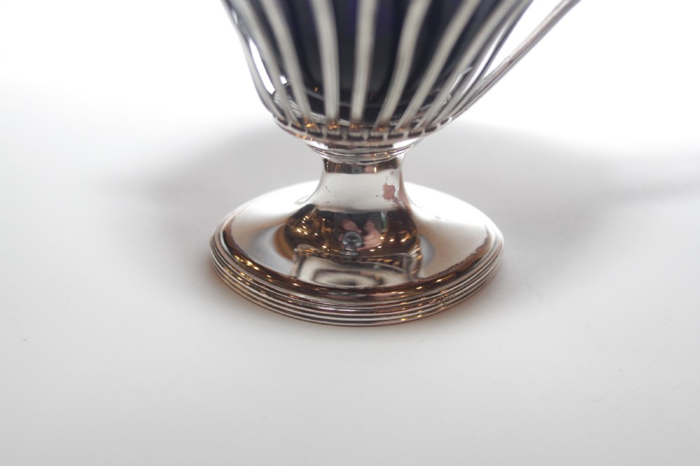 A silver-plated mustard pot with a pedestalled base, looped handle, conical lid, and removable cobalt blue glass liner. View VI