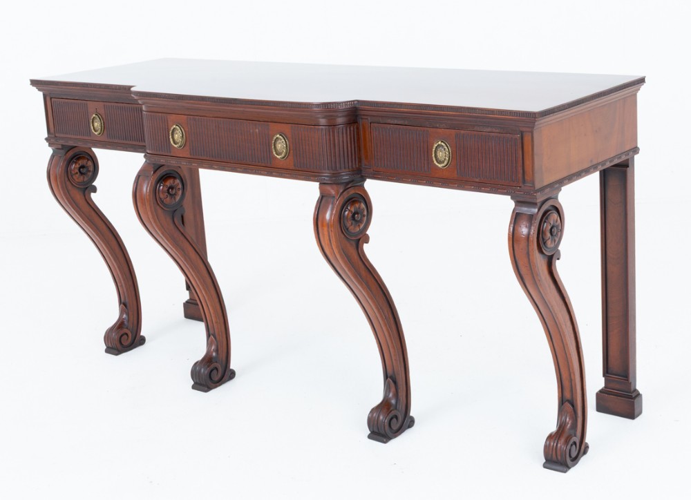 A Georgian Revival mahogany server featuring three fluted front drawers with circular brass handles and four carved scroll legs.