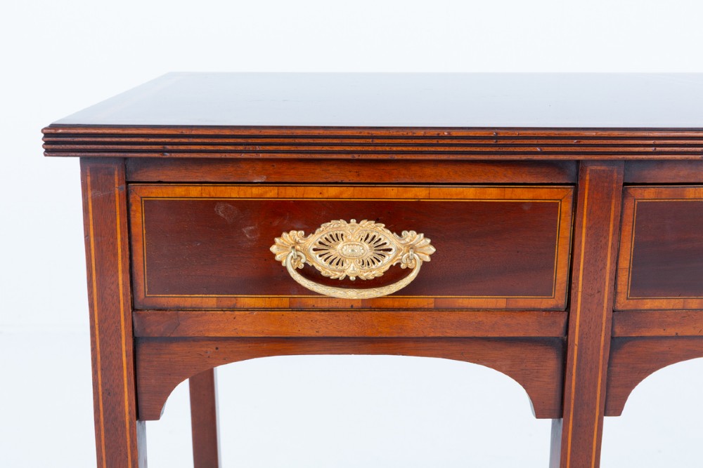 A Sheraton Revival mahogany server featuring three drawers with brass handles, decorative string inlay, arched spandrels, and four slender tapered legs. View III