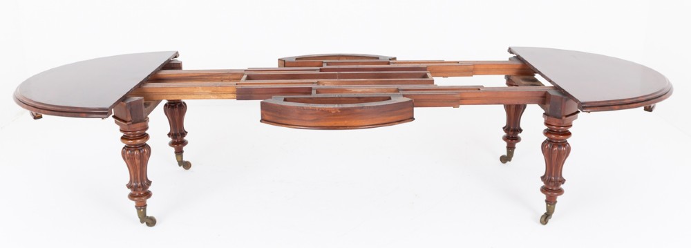 Large Victorian mahogany extending dining table featuring rounded ends, multiple removable leaves, turned fluted legs, and brass castors. View IV