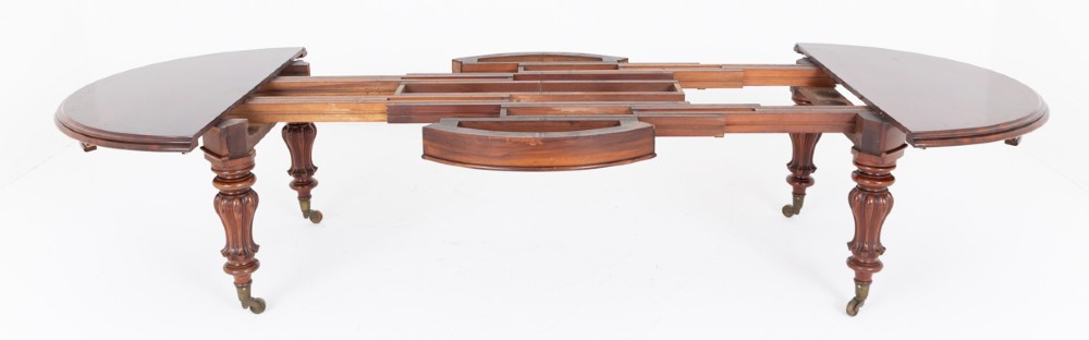 Large Victorian mahogany extending dining table featuring rounded ends, multiple removable leaves, turned fluted legs, and brass castors. View V