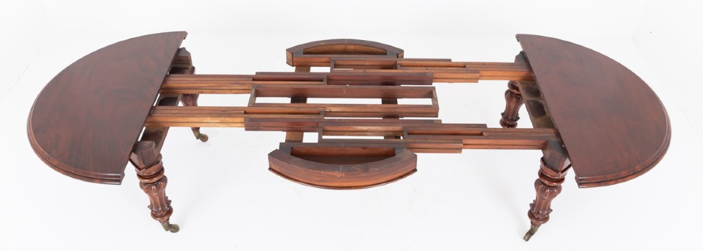 Large Victorian mahogany extending dining table featuring rounded ends, multiple removable leaves, turned fluted legs, and brass castors. View VI