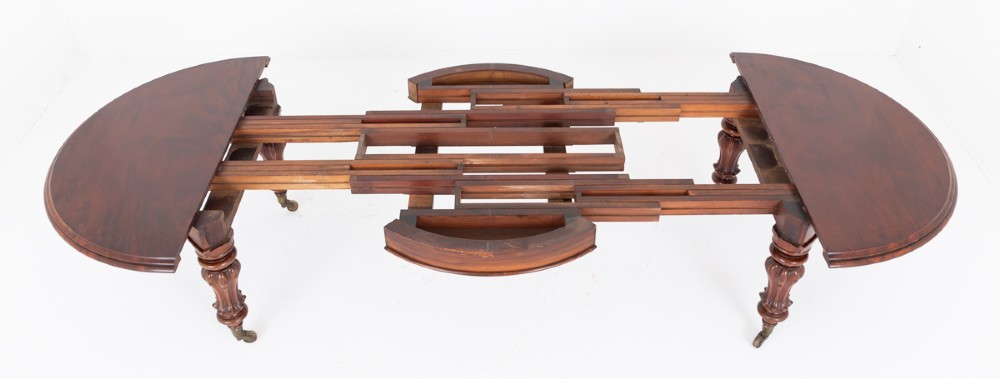 Large Victorian mahogany extending dining table featuring rounded ends, multiple removable leaves, turned fluted legs, and brass castors. View VII