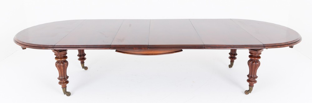 Large Victorian mahogany extending dining table featuring rounded ends, multiple removable leaves, turned fluted legs, and brass castors.
