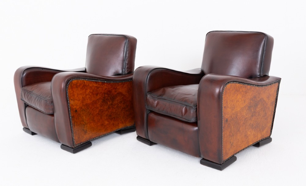 A pair of Art Deco club chairs upholstered in brown leather with burr walnut side panels and studded trim.