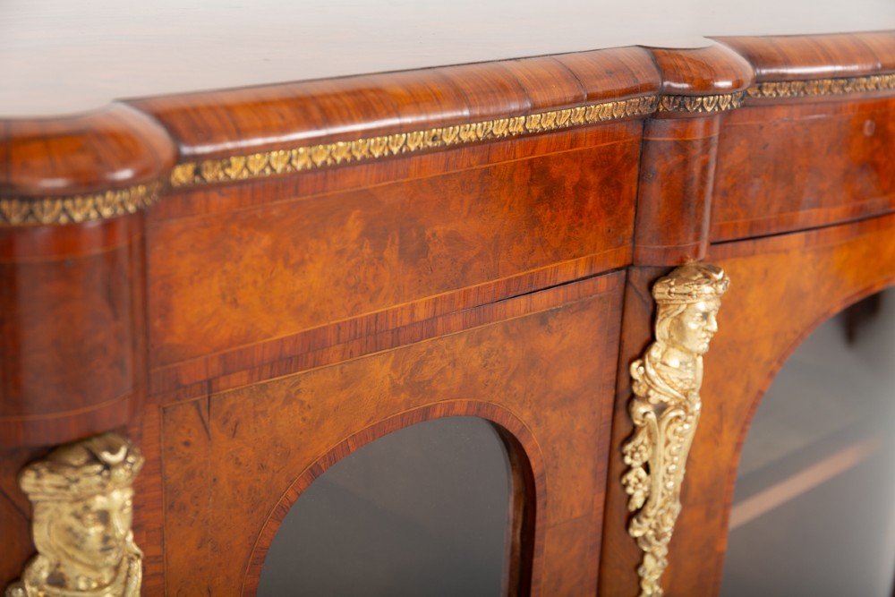A Victorian burr walnut credenza featuring three arched glazed doors, intricate gilt ormolu mounts, and a solid plinth base. View V