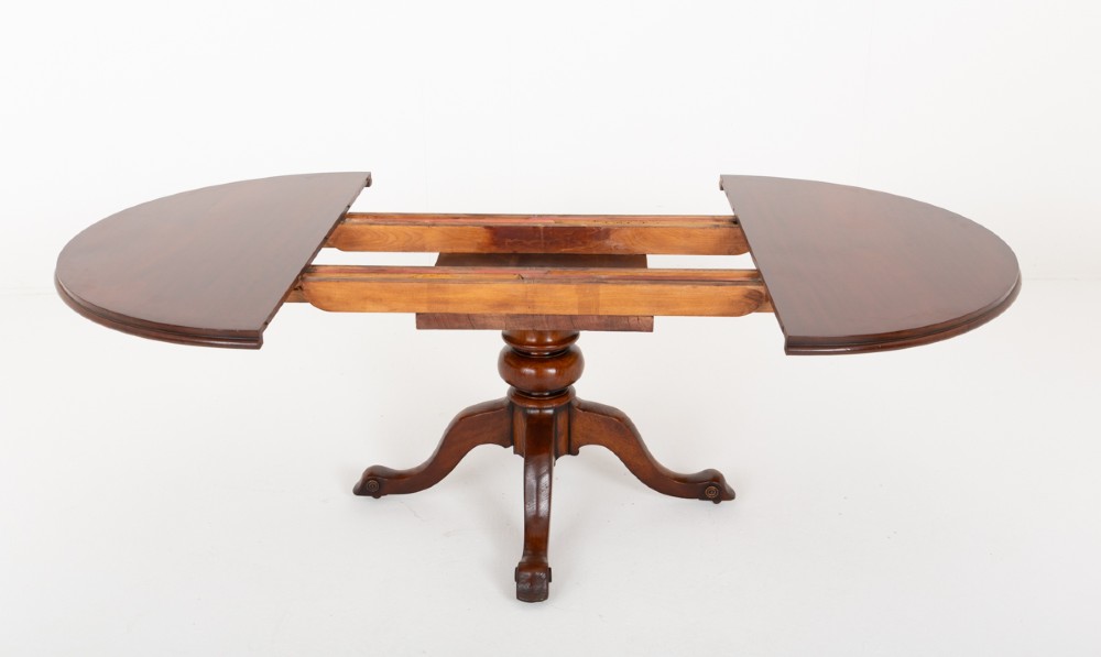 An antique Victorian mahogany extending dining table featuring an oval top, removable centre leaf, and a carved central pedestal base with splayed legs. View IV