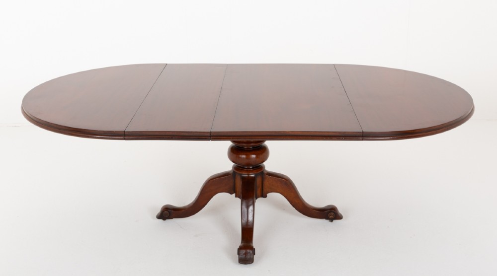 An antique Victorian mahogany extending dining table featuring an oval top, removable centre leaf, and a carved central pedestal base with splayed legs. View V