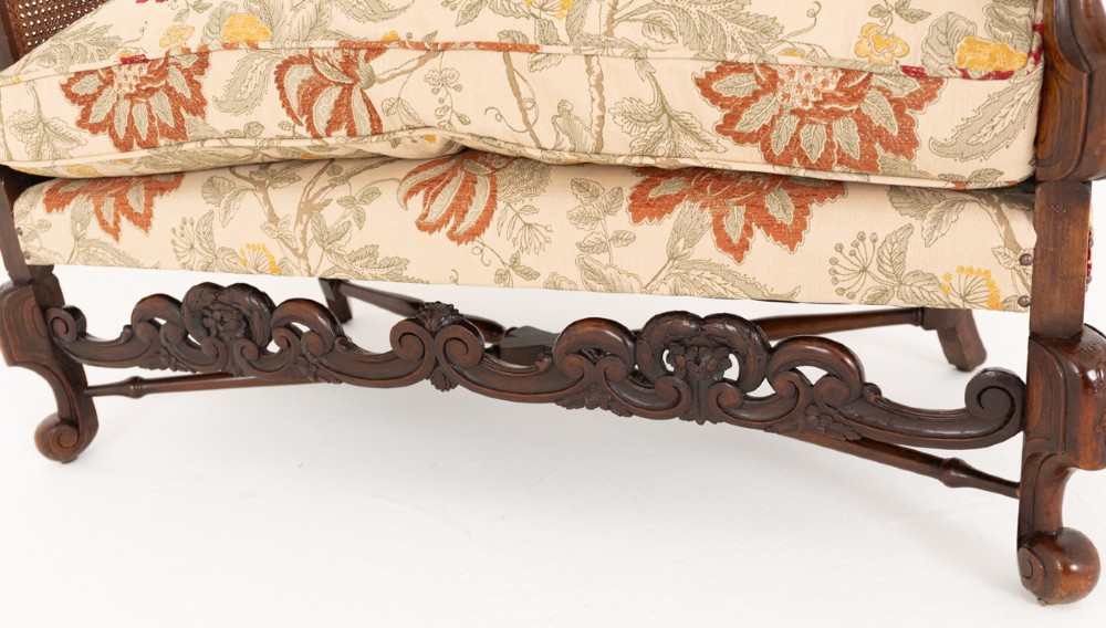 A three-piece Carolean style seating suite comprising a settee and two matching armchairs with woven cane backrests, carved scroll stretchers, and floral fabric seat cushions. View VII
