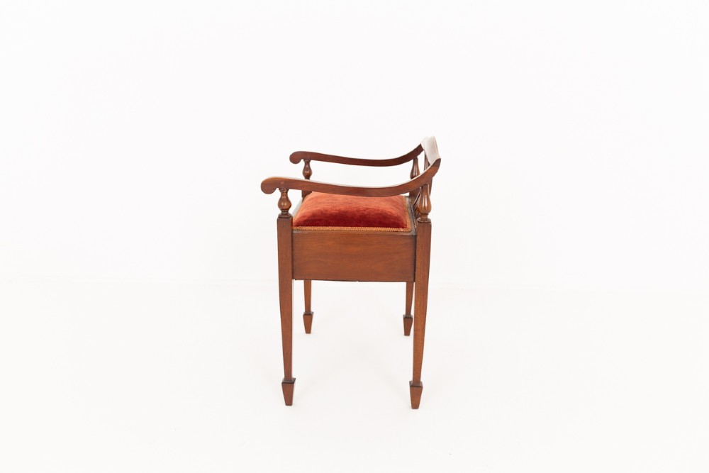 A Sheraton Revival mahogany piano stool featuring a slatted curved backrest, curved arms, red velvet cushioned seat, and square tapered legs with inlaid boxwood stringing. View III