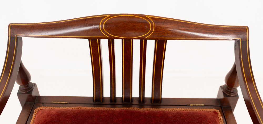 A Sheraton Revival mahogany piano stool featuring a slatted curved backrest, curved arms, red velvet cushioned seat, and square tapered legs with inlaid boxwood stringing. View VI