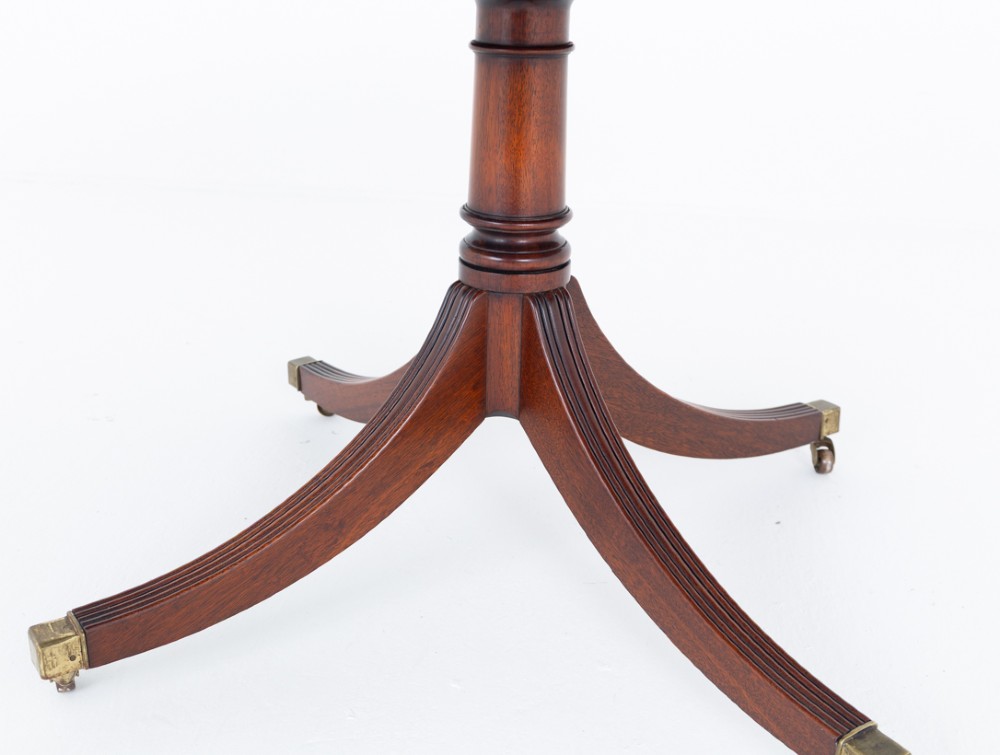 An extendable Regency Revival oval mahogany dining table with a central turned pedestal support, four reeded swept legs, and brass castors. View III