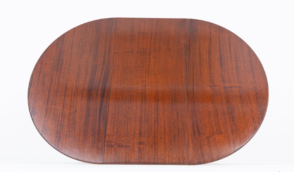 An extendable Regency Revival oval mahogany dining table with a central turned pedestal support, four reeded swept legs, and brass castors. View VIII