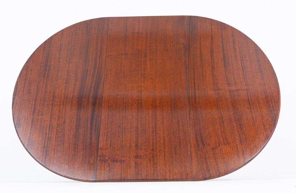 An extendable Regency Revival oval mahogany dining table with a central turned pedestal support, four reeded swept legs, and brass castors. View IX