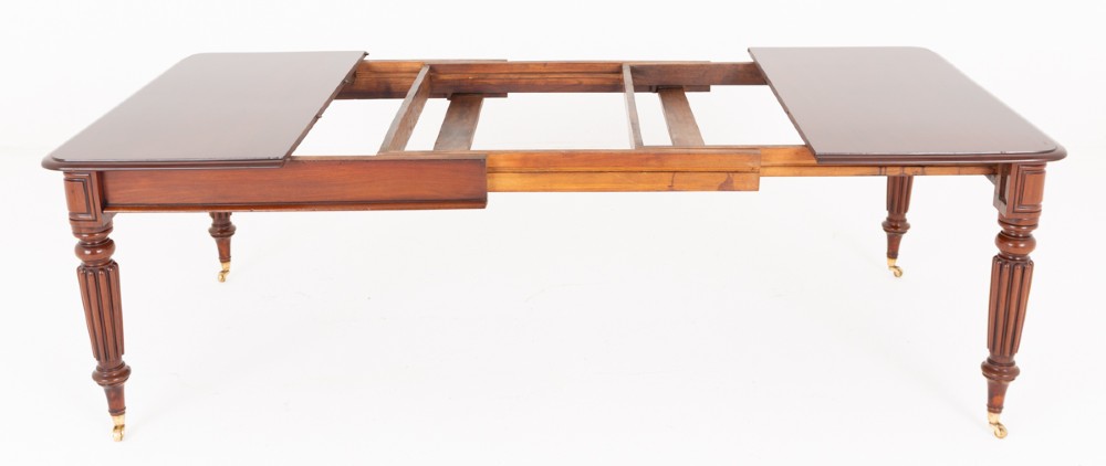 A Regency mahogany extending dining table with two removable leaves, turned reeded legs, and brass castors. View III
