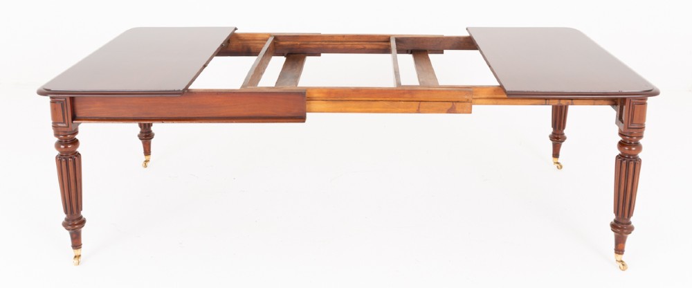 A Regency mahogany extending dining table with two removable leaves, turned reeded legs, and brass castors. View IV