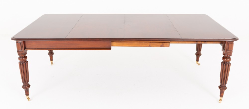 A Regency mahogany extending dining table with two removable leaves, turned reeded legs, and brass castors. View V