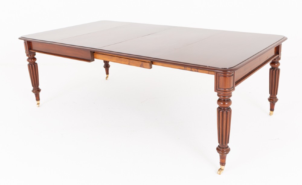 A Regency mahogany extending dining table with two removable leaves, turned reeded legs, and brass castors. View VI