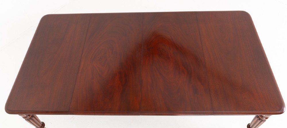 A Regency mahogany extending dining table with two removable leaves, turned reeded legs, and brass castors. View VII