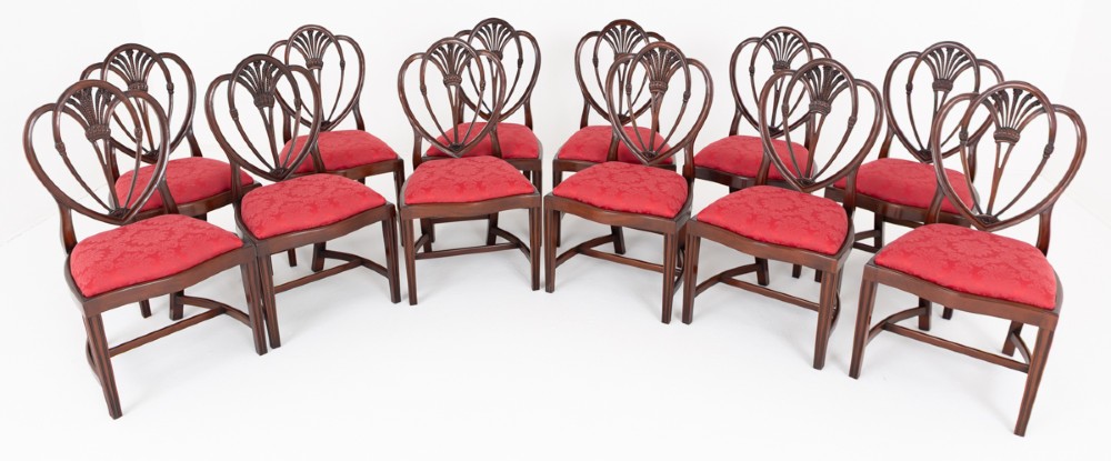 A set of twelve mahogany dining chairs with carved Prince of Wales plume backs and red damask fabric seats arranged in a arc.
