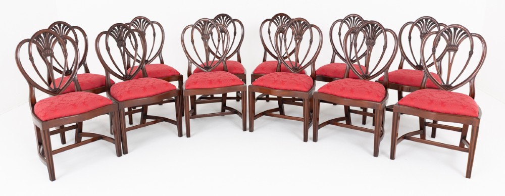 A set of twelve mahogany dining chairs with carved Prince of Wales plume backs and red damask fabric seats arranged in a arc. View II