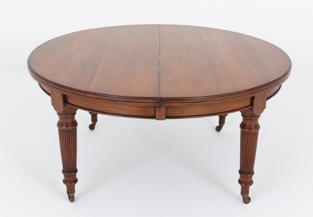 An extended oval walnut dining table with fluted turned legs ending in brass castors. View II
