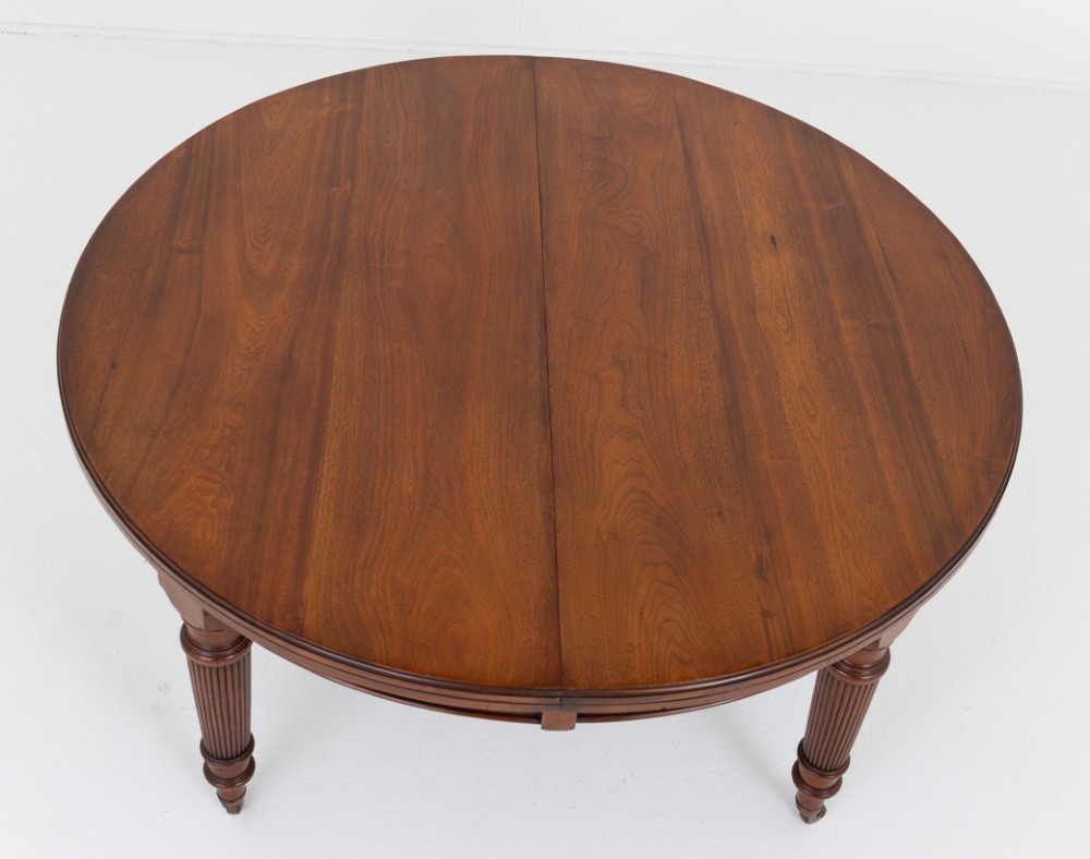 An extended oval walnut dining table with fluted turned legs ending in brass castors. View IV