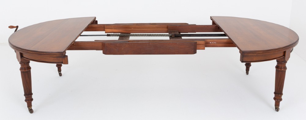 An extended oval walnut dining table with fluted turned legs ending in brass castors. View V