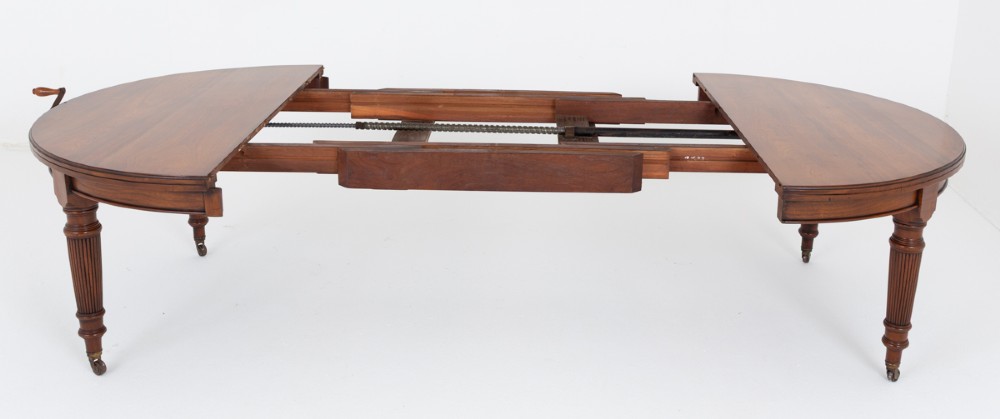 An extended oval walnut dining table with fluted turned legs ending in brass castors. View VI