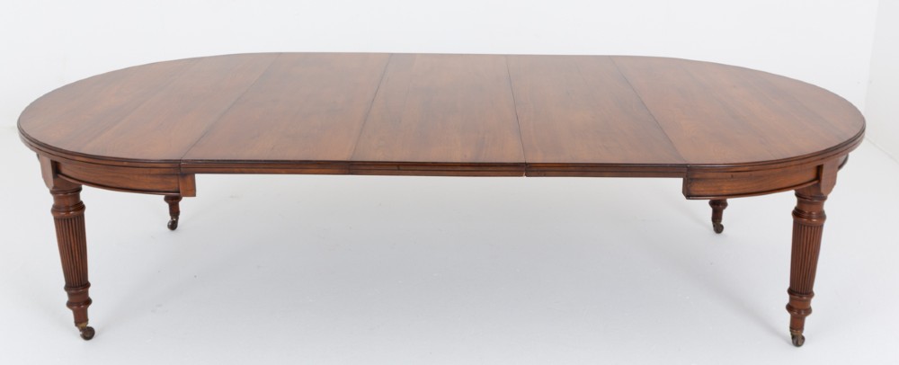 An extended oval walnut dining table with fluted turned legs ending in brass castors. View VII
