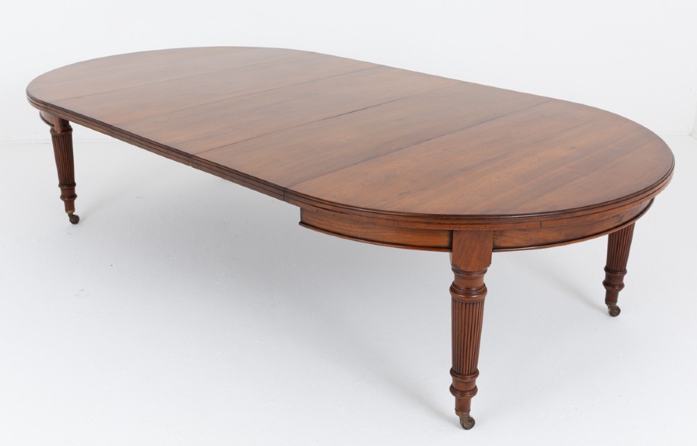 An extended oval walnut dining table with fluted turned legs ending in brass castors.