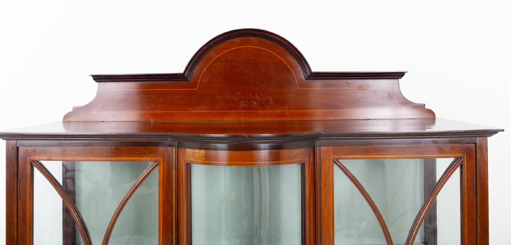 A Sheraton Revival mahogany display cabinet featuring an arched pediment, glass-front doors with geometric glazing bars, marquetry inlay panels, and a lower shelf supported by slender legs. View V