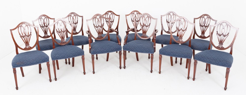 A set of twelve mahogany Hepplewhite style dining chairs with shield backs, carved urn splats, and blue patterned upholstered seats.