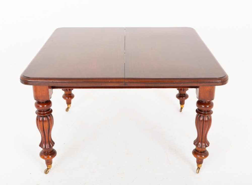 A Victorian mahogany extending dining table with two insertable leaves, fluted turned legs, and brass castors. View II