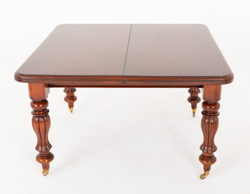 A Victorian mahogany extending dining table with two insertable leaves, fluted turned legs, and brass castors. View III