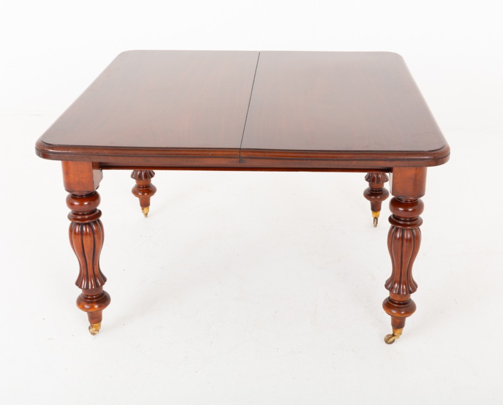 A Victorian mahogany extending dining table with two insertable leaves, fluted turned legs, and brass castors. View IV