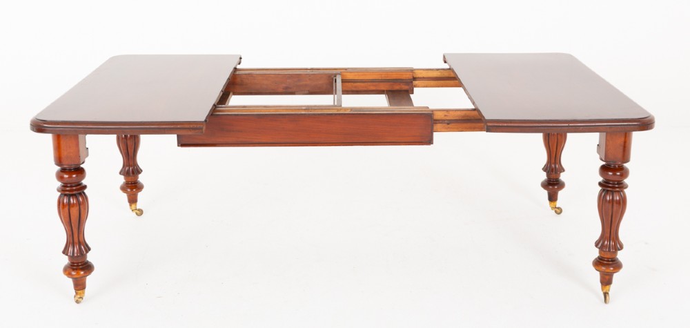 A Victorian mahogany extending dining table with two insertable leaves, fluted turned legs, and brass castors. View VII