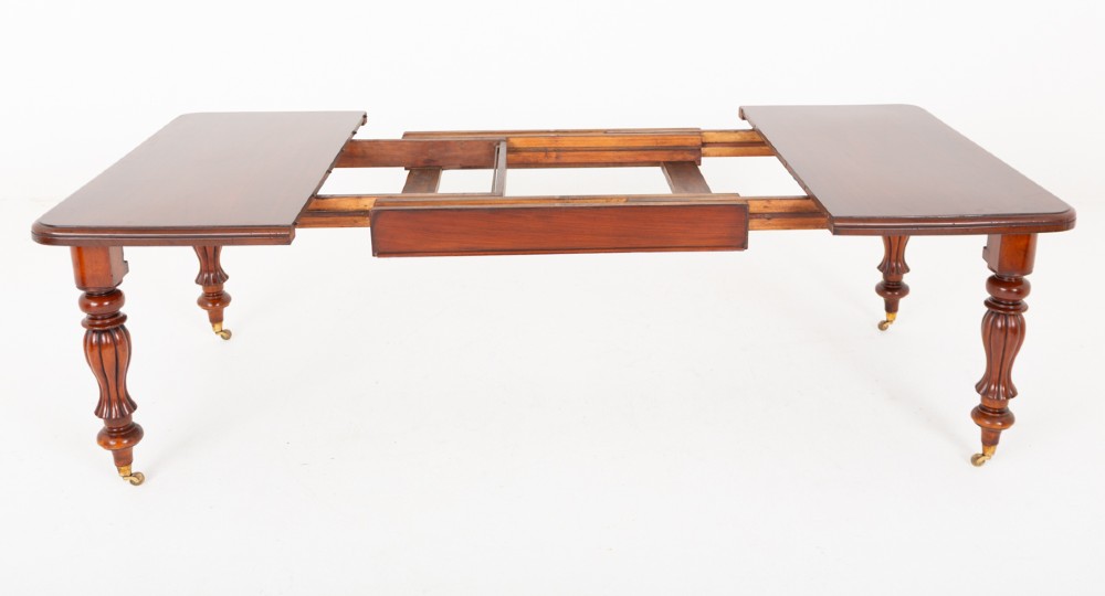 A Victorian mahogany extending dining table with two insertable leaves, fluted turned legs, and brass castors. View IX
